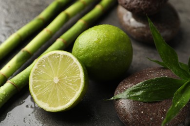Photo of Spa composition with wet limes, pebble stones, bamboo leaves and stems on grey table, closeup
