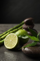 Photo of Spa composition with wet limes, pebble stones, bamboo leaves and stems on grey table against black background, closeup