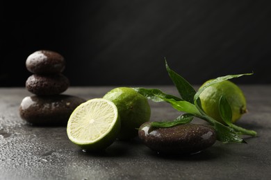 Photo of Spa composition with wet limes, pebble stones and bamboo leaves on grey table against black background, closeup