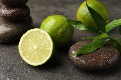 Photo of Spa composition with wet limes, pebble stones and bamboo leaves on grey table, closeup