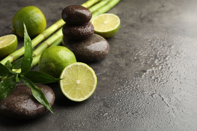 Photo of Spa composition with wet limes, pebble stones, bamboo leaves and stems on grey table, closeup. Space for text