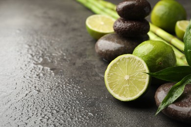 Photo of Spa composition with wet limes, pebble stones, bamboo leaves and stems on grey table, closeup. Space for text