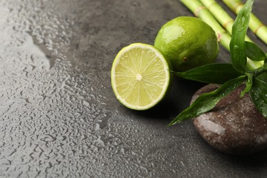 Photo of Spa composition with wet limes, pebble stone, bamboo leaves and stems on grey table, closeup. Space for text