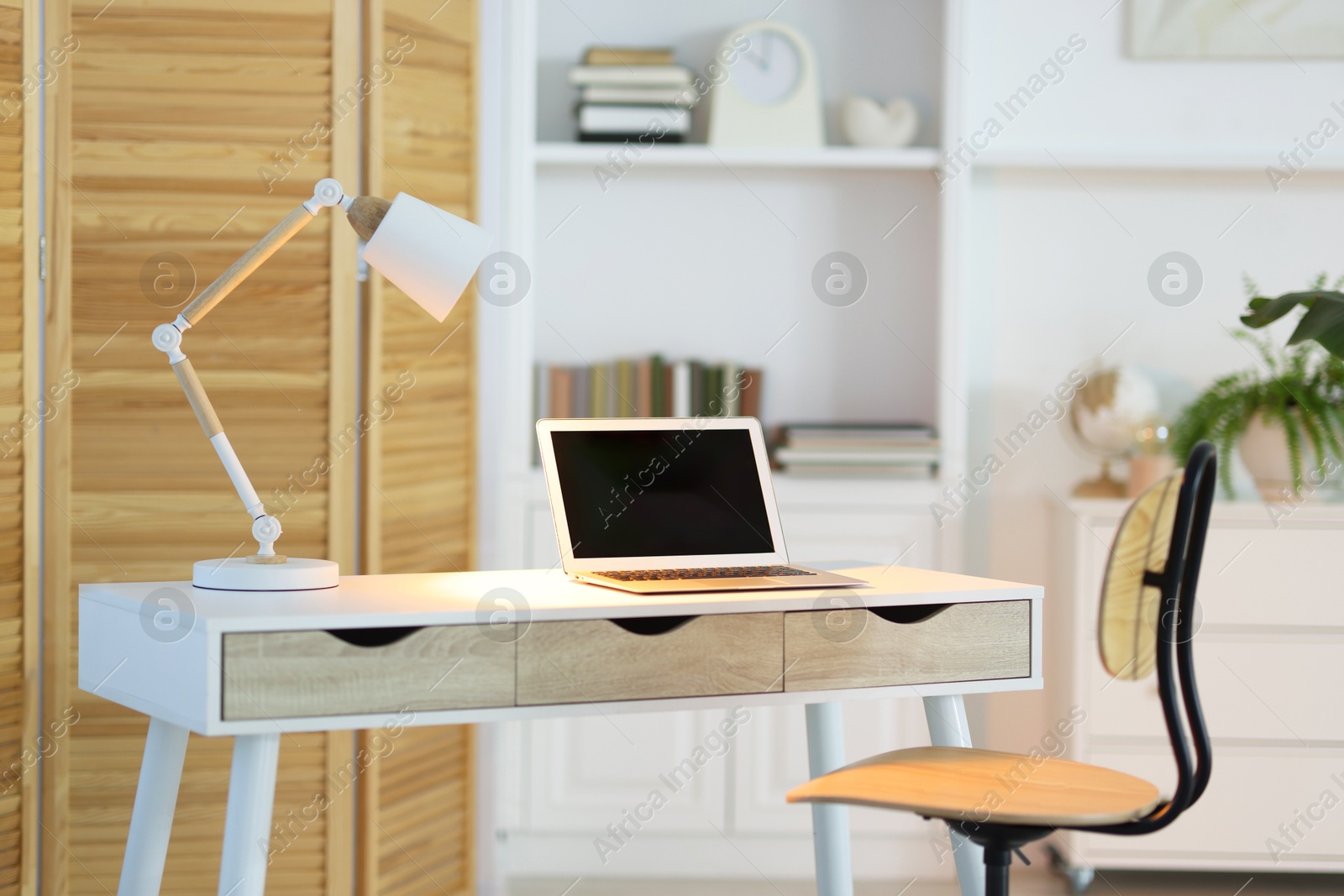 Photo of Comfortable workplace with laptop and lamp on table indoors