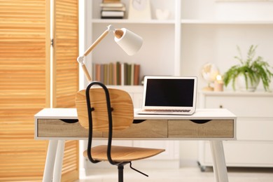 Comfortable workplace with laptop and lamp on table indoors