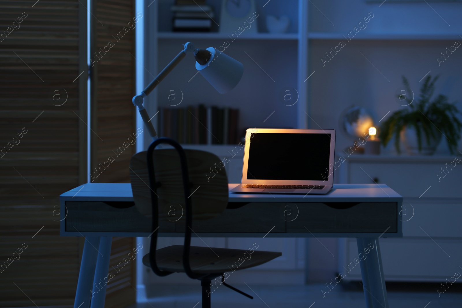 Photo of Comfortable workplace with laptop and lamp on table indoors