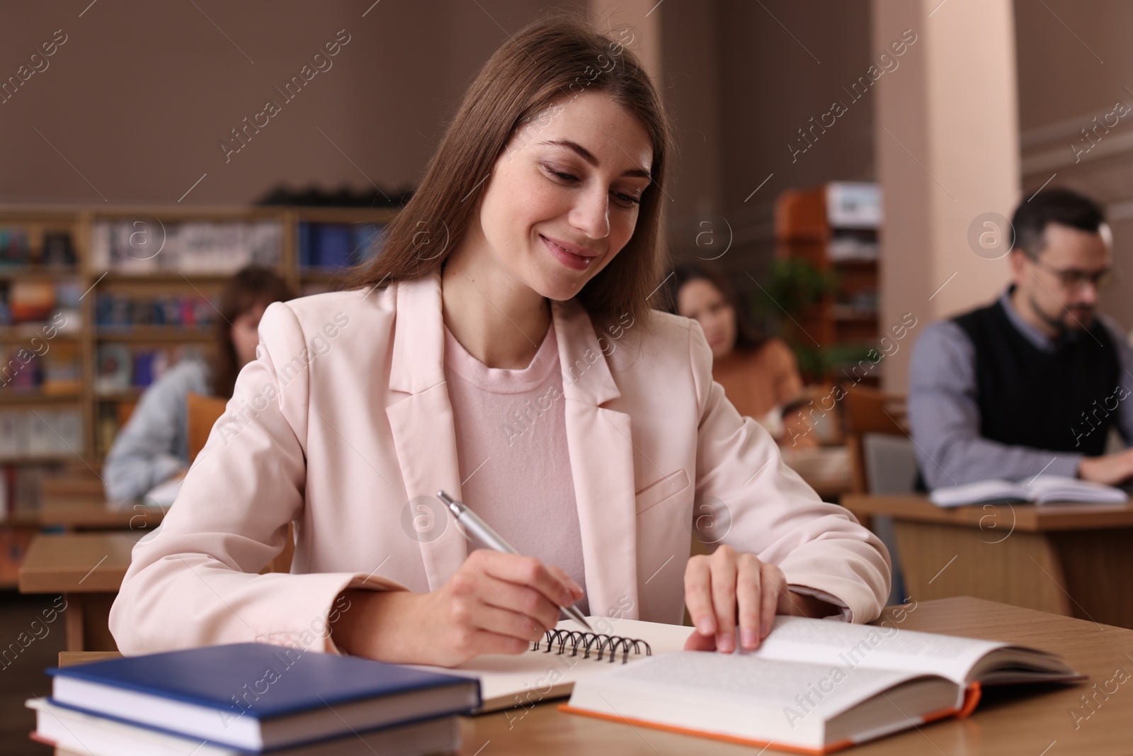 Photo of Beautiful woman reading book and taking notes at desk in public library