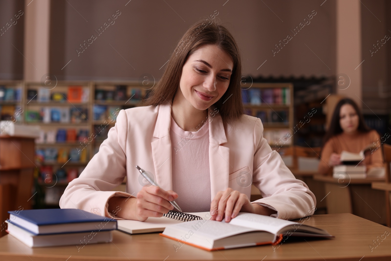 Photo of Beautiful woman reading book and taking notes at desk in public library