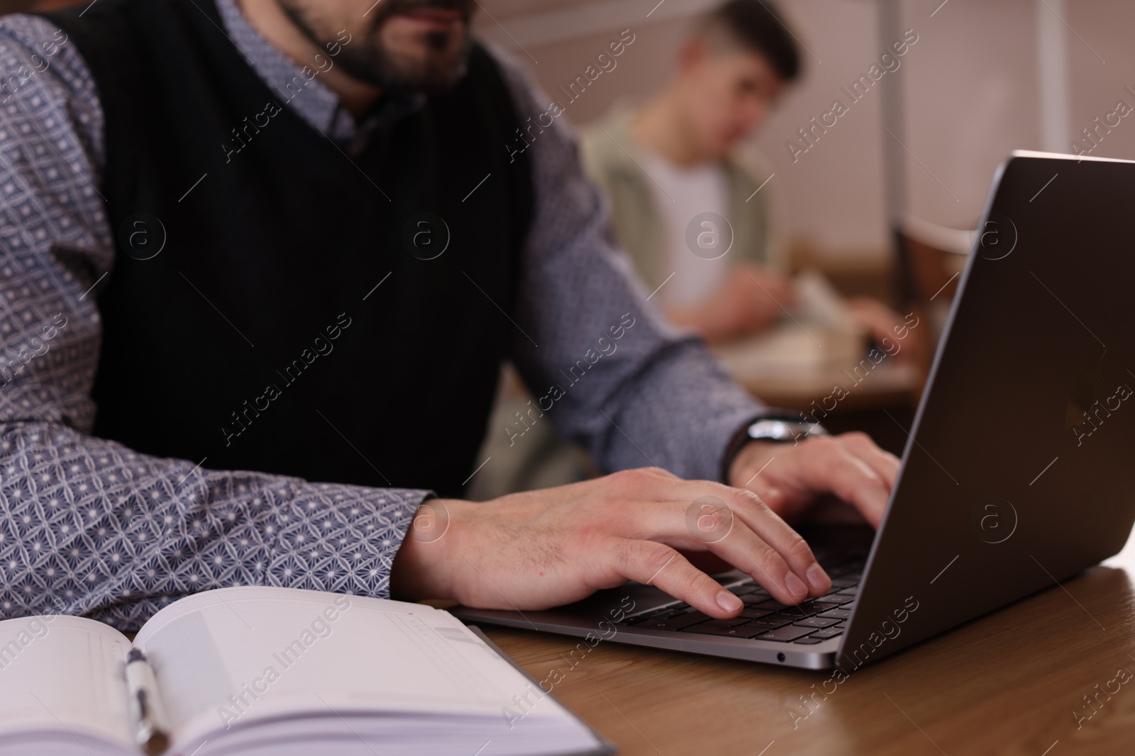 Photo of Man typing on laptop near book at desk in library, closeup