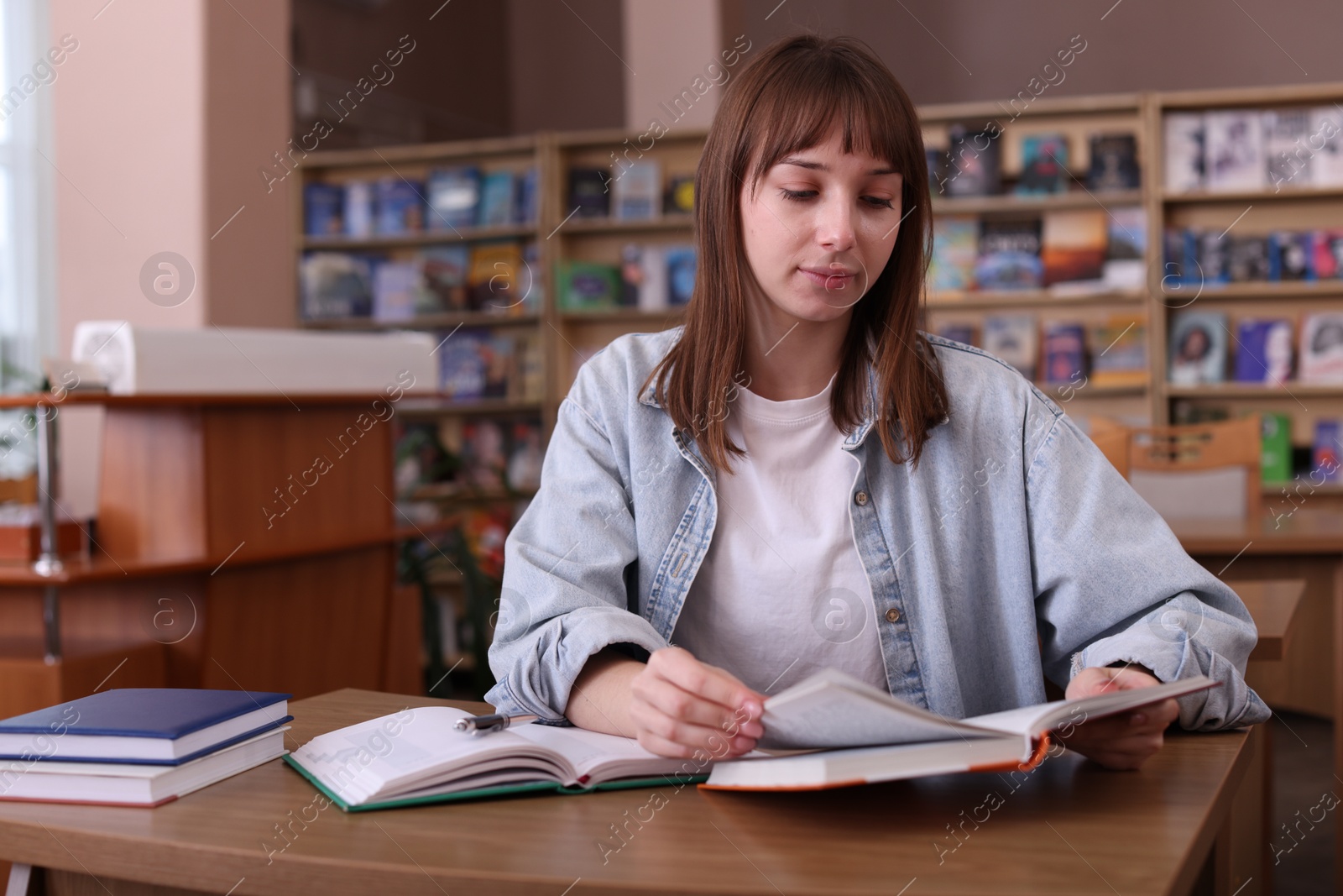 Photo of Beautiful woman reading book at desk in public library