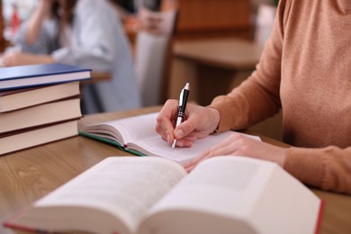 Photo of Woman reading book and taking notes at desk in library, closeup