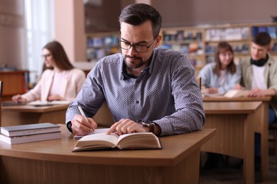 Photo of Handsome man reading book and taking notes at desk in public library