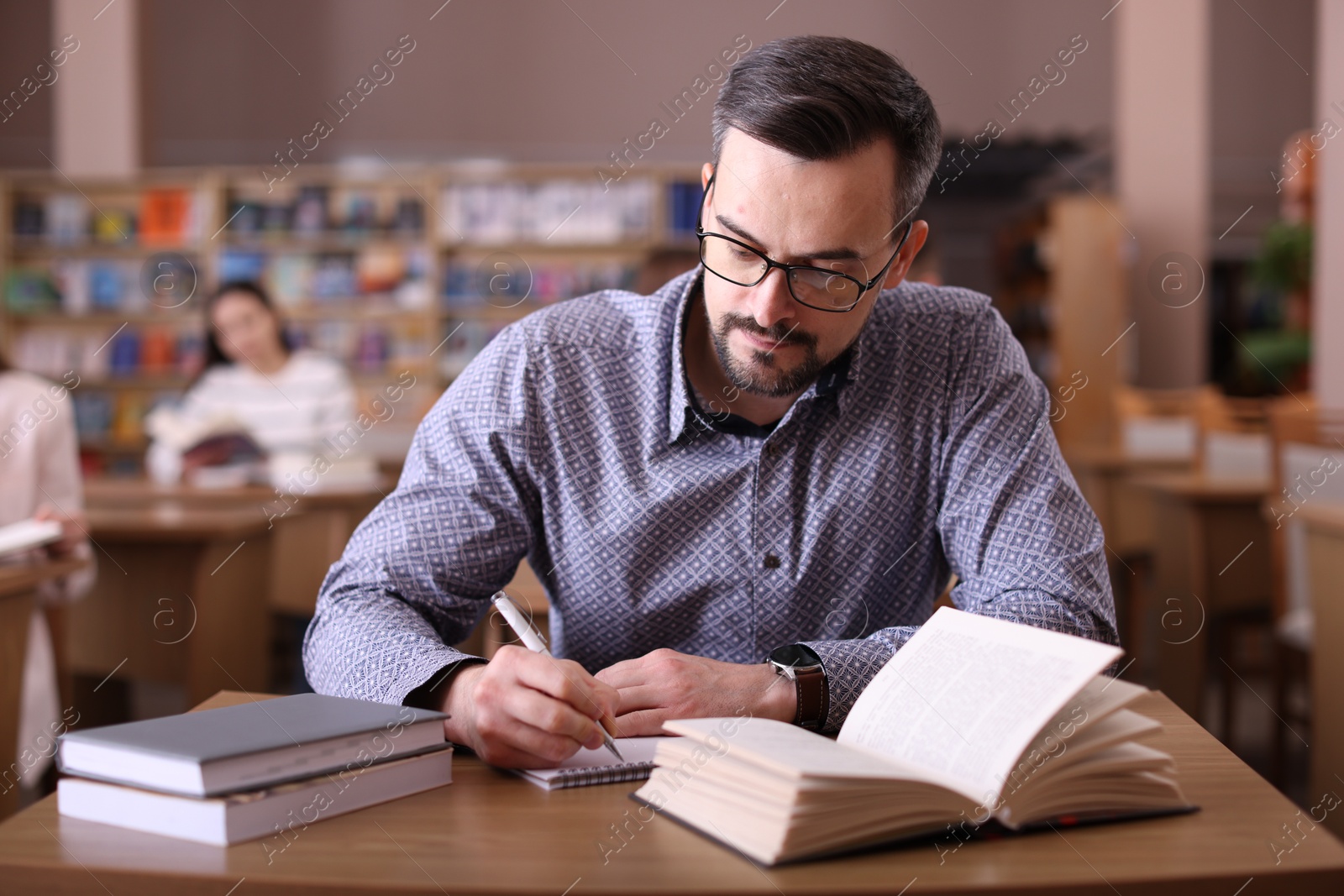 Photo of Handsome man reading book and taking notes at desk in public library