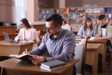 Photo of Handsome man reading book and taking notes at desk in public library