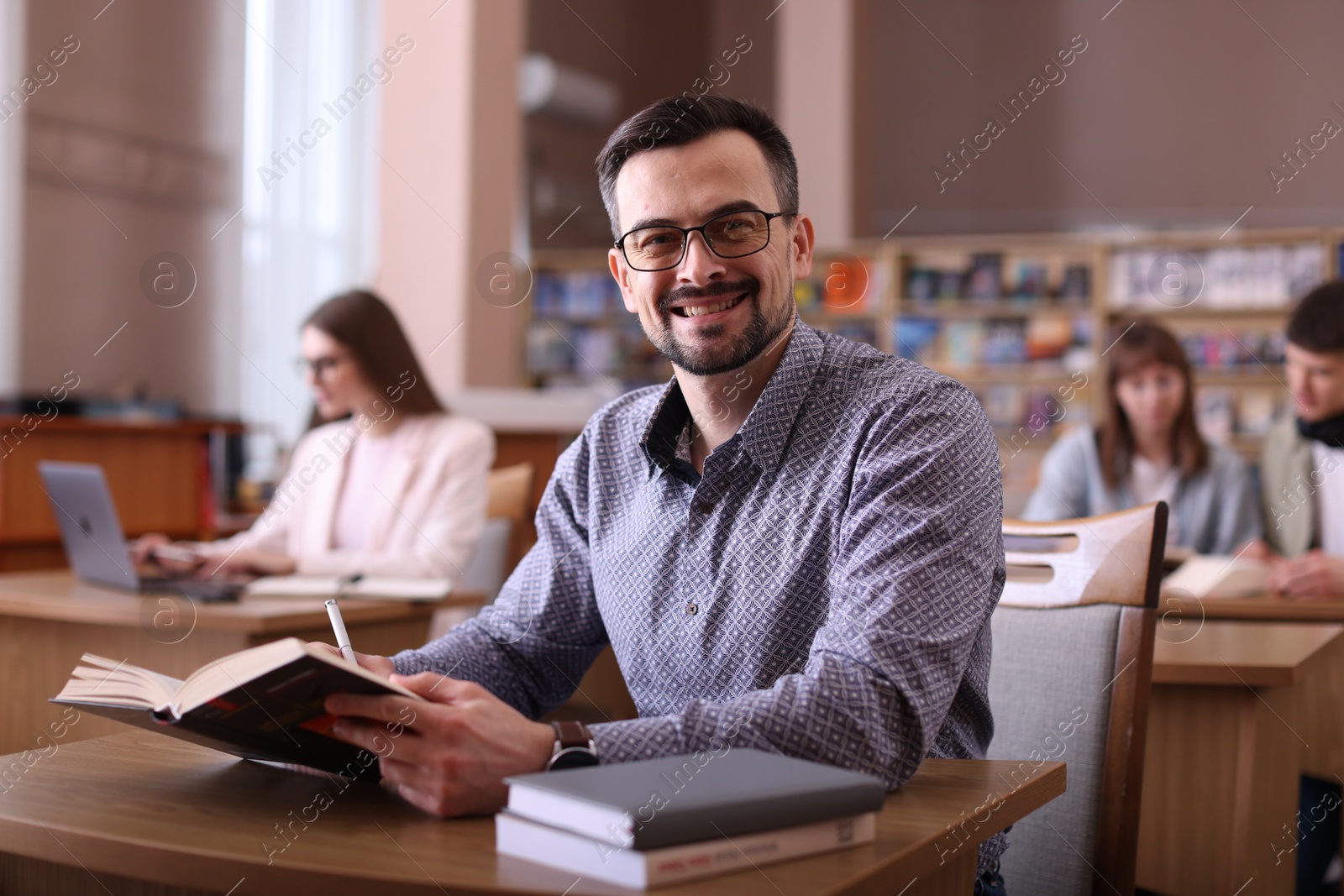 Photo of Portrait of smiling man with book at desk in public library