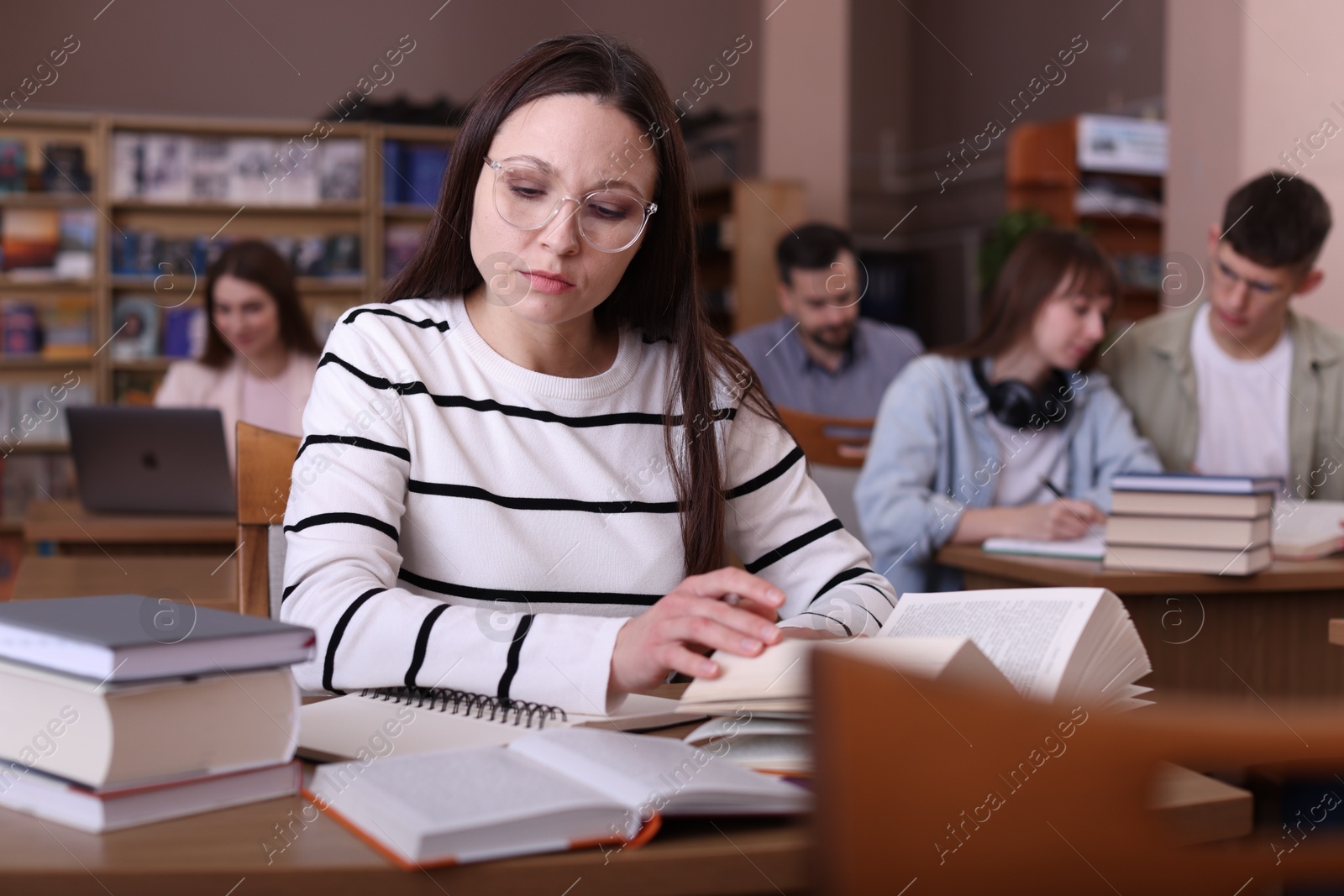 Photo of Beautiful woman reading book at desk in public library