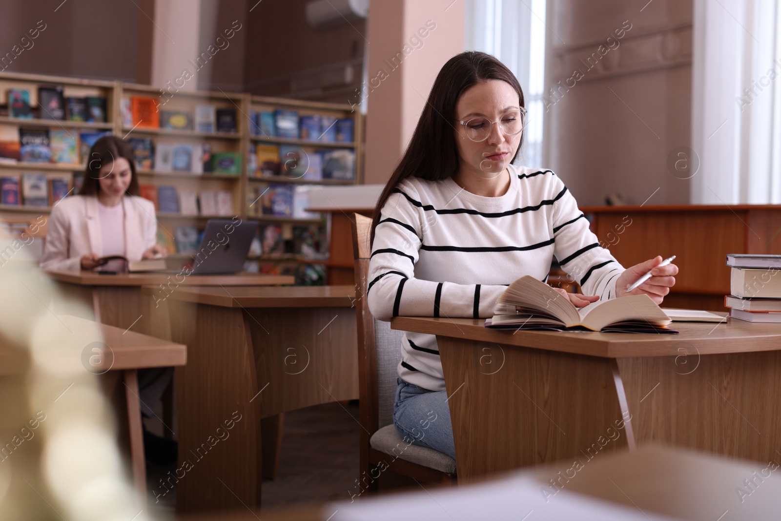 Photo of Beautiful woman reading book at desk in public library