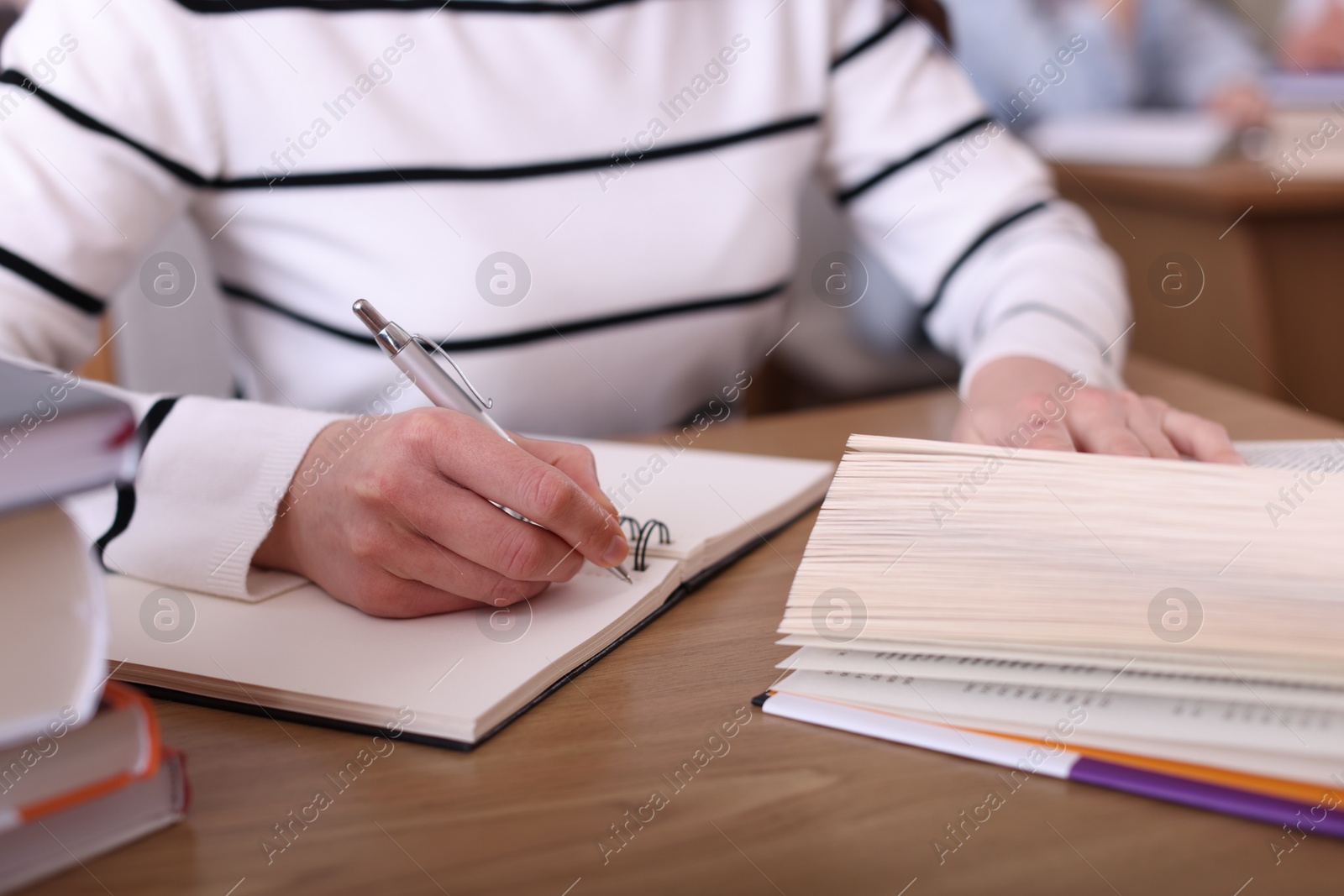 Photo of Woman reading book and taking notes at desk in library, closeup