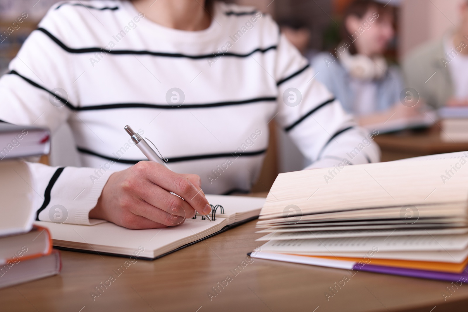 Photo of Woman reading book and taking notes at desk in library, closeup