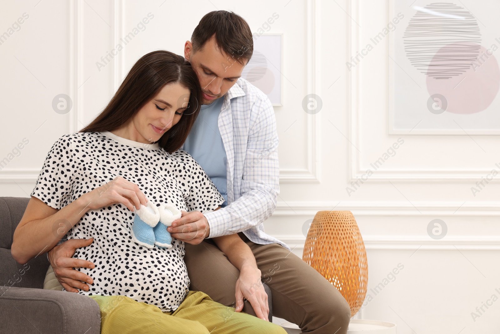 Photo of Pregnant woman and her husband with baby booties at home. Space for text