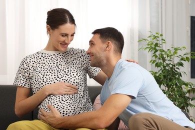 Photo of Man trying to feel baby kicks in his pregnant wife's belly on sofa at home