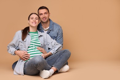 Pregnant woman and her husband on beige background. Space for text