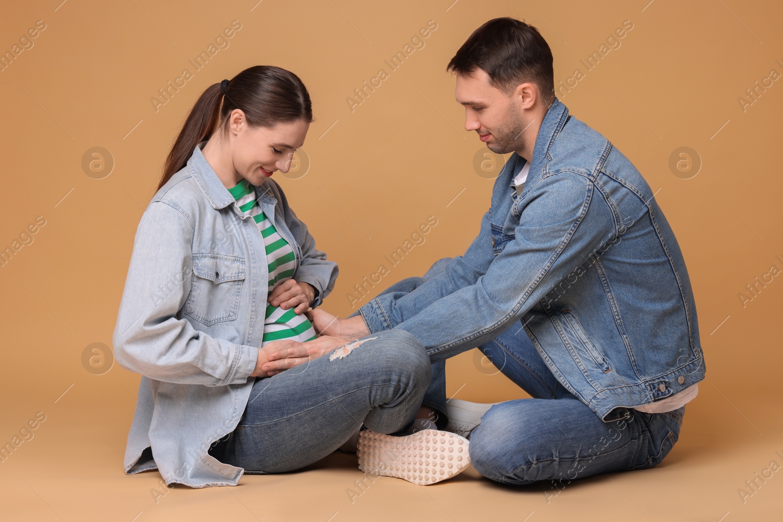 Photo of Man trying to feel baby kicks in his pregnant wife's belly on beige background