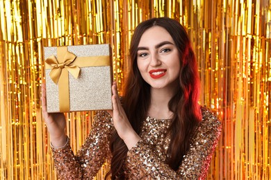 Photo of Happy young woman with gift box against golden foil curtain