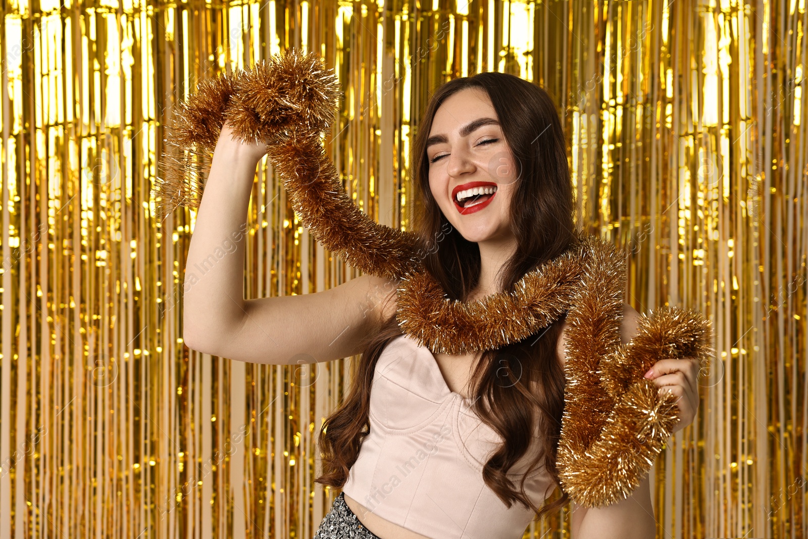 Photo of Happy young woman with tinsel against golden foil curtain