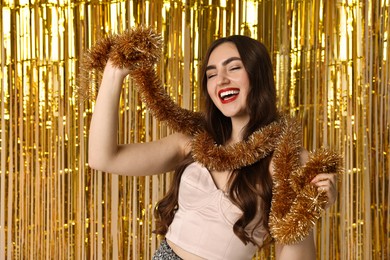 Photo of Happy young woman with tinsel against golden foil curtain