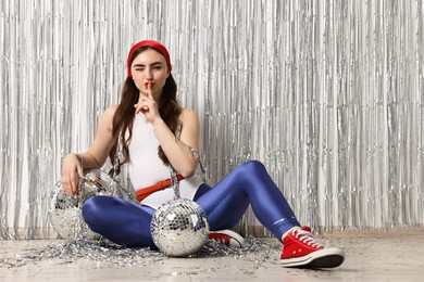 Photo of Beautiful young woman in retro outfit with disco balls against silver foil curtain indoors