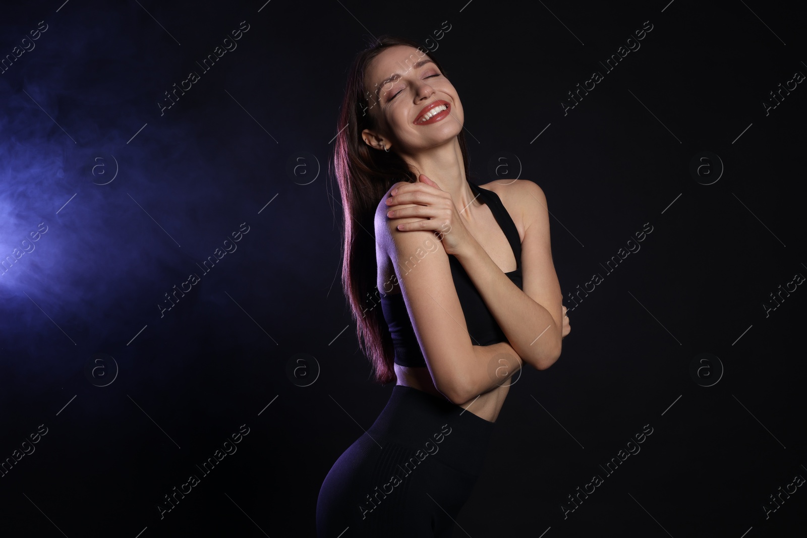 Photo of Beautiful woman in stylish sportswear on dark background with color light and smoke