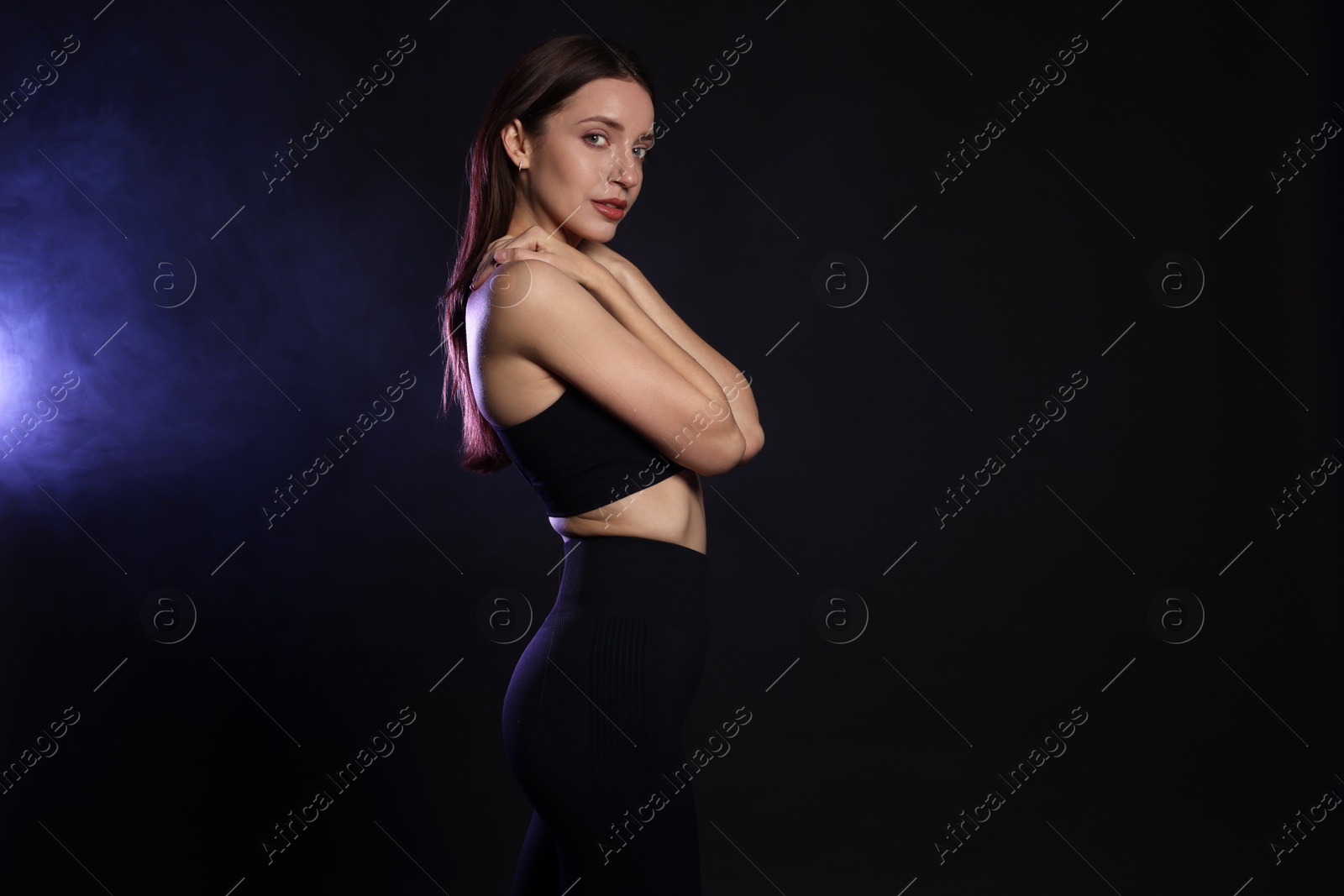 Photo of Beautiful woman in stylish sportswear on dark background with color light and smoke. Space for text