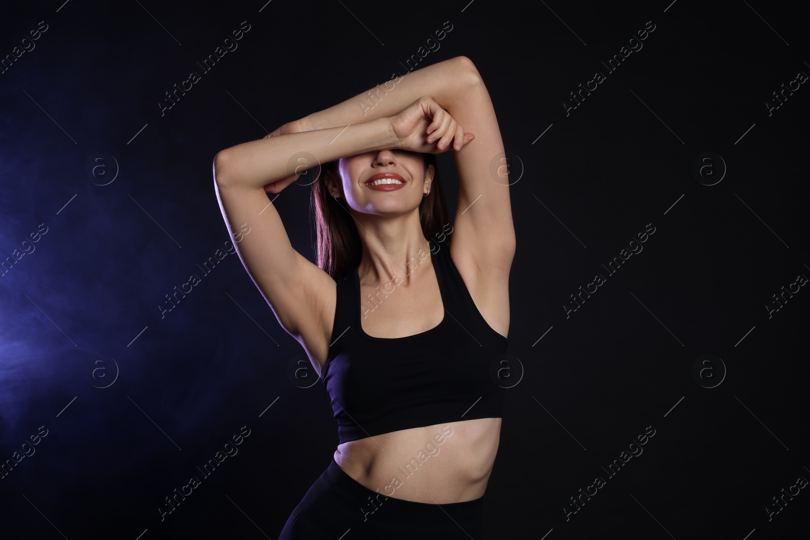 Photo of Beautiful woman in stylish sportswear on dark background with color light and smoke