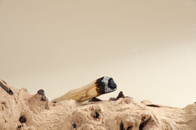 Photo of Smoldering palo santo stick and snag on beige background, closeup. Space for text