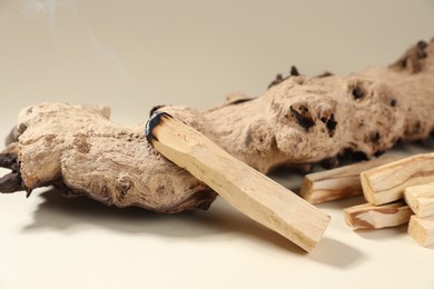 Photo of Smoldering palo santo stick and snag on beige background, closeup