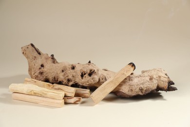 Photo of Palo santo sticks and smoldering one near snag on beige background