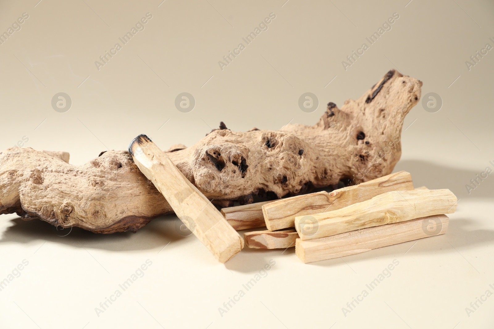 Photo of Palo santo sticks and smoldering one near snag on beige background