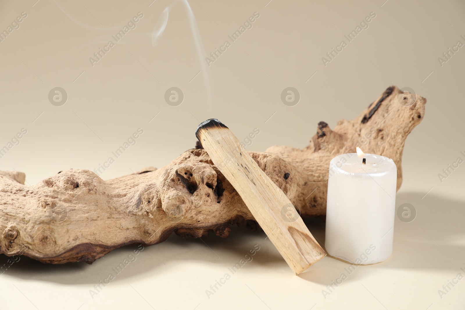 Photo of Smoldering palo santo stick, snag and burning candle on beige background, closeup