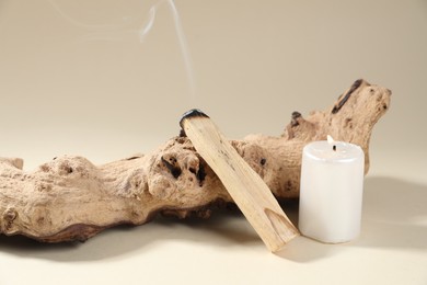 Photo of Smoldering palo santo stick, snag and burning candle on beige background, closeup