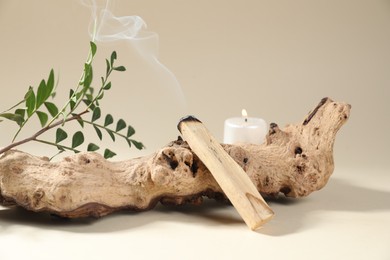 Photo of Smoldering palo santo stick, snag, green branch and burning candle on beige background, closeup