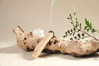 Photo of Smoldering palo santo stick, snag, green branch and burning candle on beige background