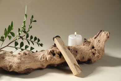 Photo of Smoldering palo santo stick, snag, green branch and burning candle on beige background, closeup