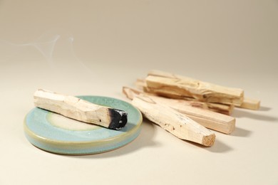 Photo of Palo santo sticks and smoldering one on beige background, closeup