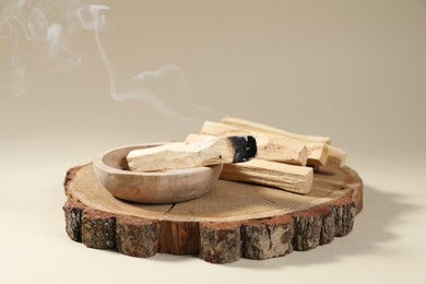 Photo of Palo santo sticks and smoldering one on beige background, closeup