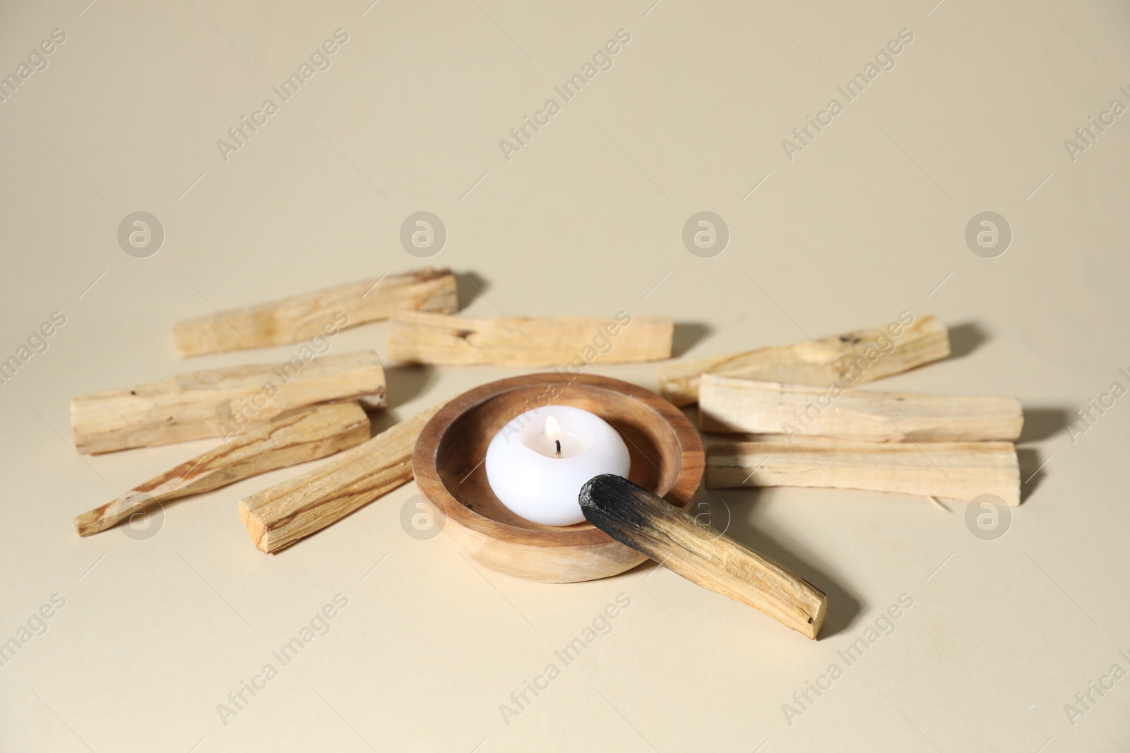 Photo of Palo santo sticks, burnt one and burning candle on beige background, closeup