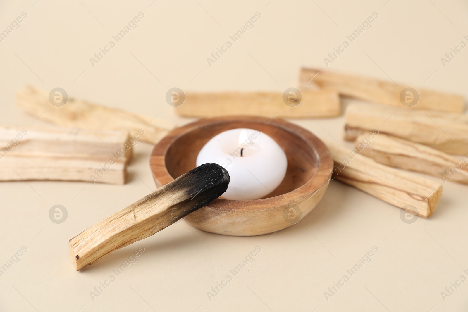 Photo of Palo santo sticks, burnt one and burning candle on beige background, closeup