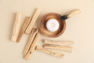 Photo of Palo santo sticks, burnt one and burning candle on beige background, flat lay