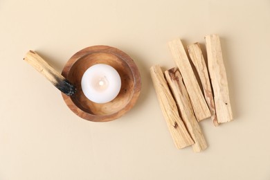 Photo of Palo santo sticks, burnt one and burning candle on beige background, flat lay