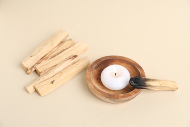 Photo of Palo santo sticks, burnt one and burning candle on beige background, closeup